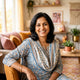 A friendly South Asian woman smiling in a bright, modern, warm-toned living room, representing a satisfied customer.